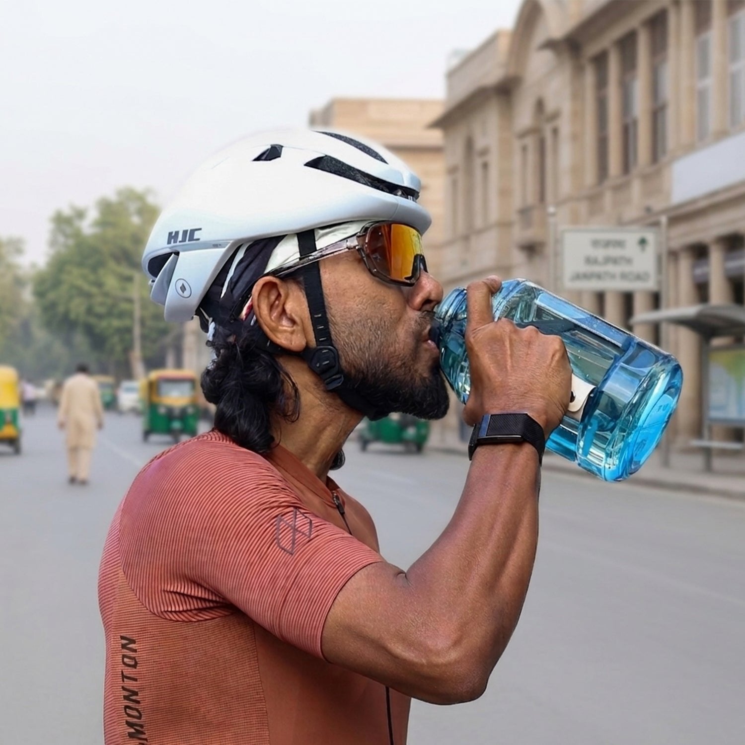 A cyclist in a helmet drinking from HydroBeast at a city roadside