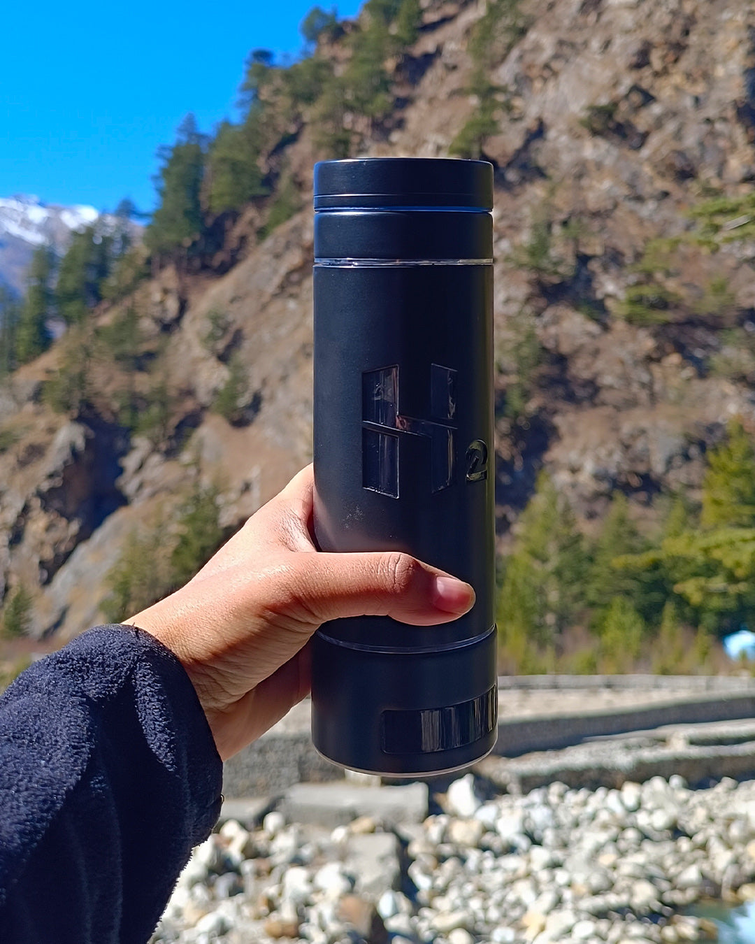 The bottle held up against a mountain valley on a morning hike